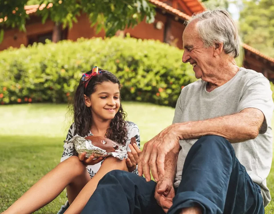 A grandfather and granddaughter sitting on the grass eating chocolate